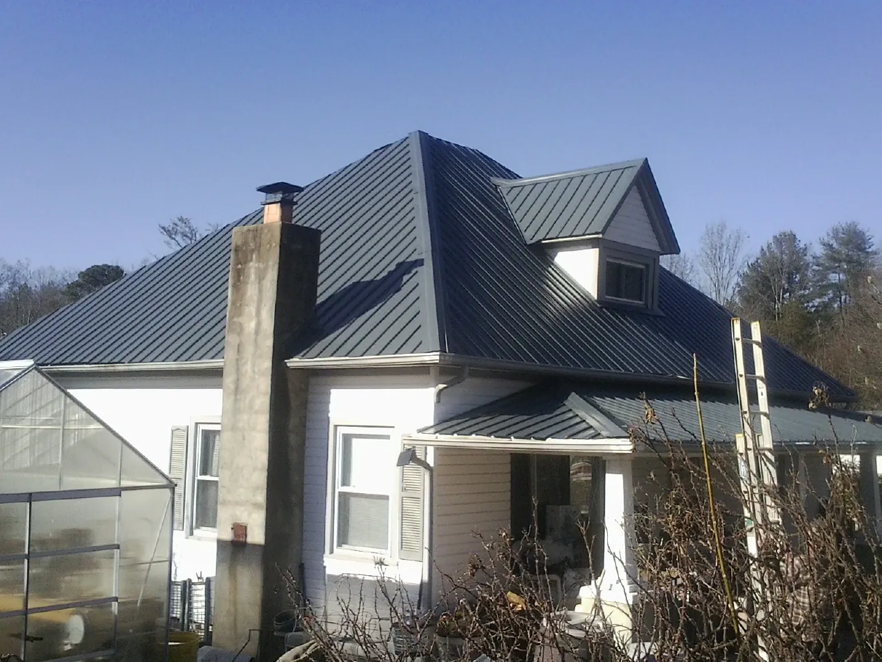 Dark blue standing seam metal roof on a white farmhouse with dormer — Slate & Tile Roof Repair by Roofing Brothers in Hatch