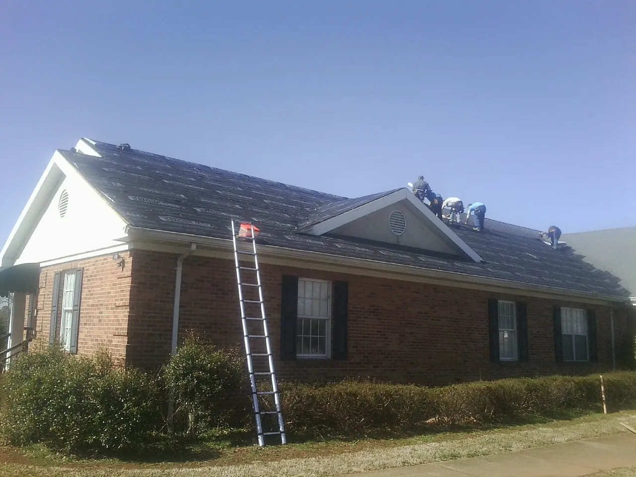 Crew tearing shingles off a brick ranch roof with a ladder set — Metal Roof Repair work by our crew in Hatch