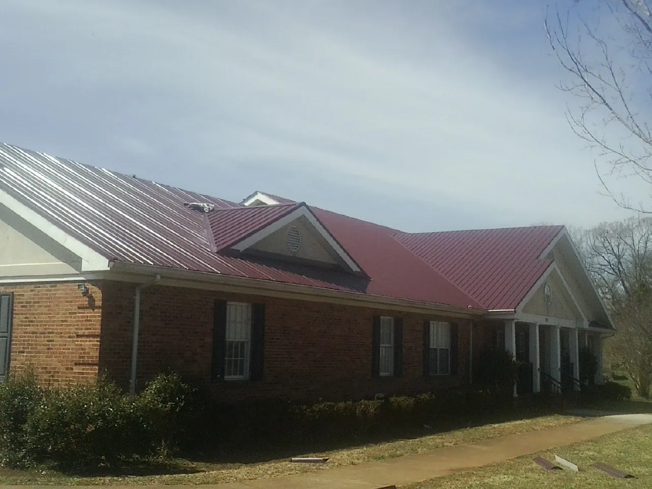 Red metal roof with gabled entries on a long brick building, from a Hail Damage Roof Repair job in Hatch
