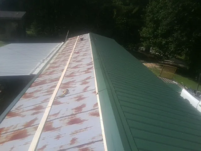 Old rusted panels beside newly installed green metal roofing — Wind Damage Roof Repair by Roofing Brothers in Hatch