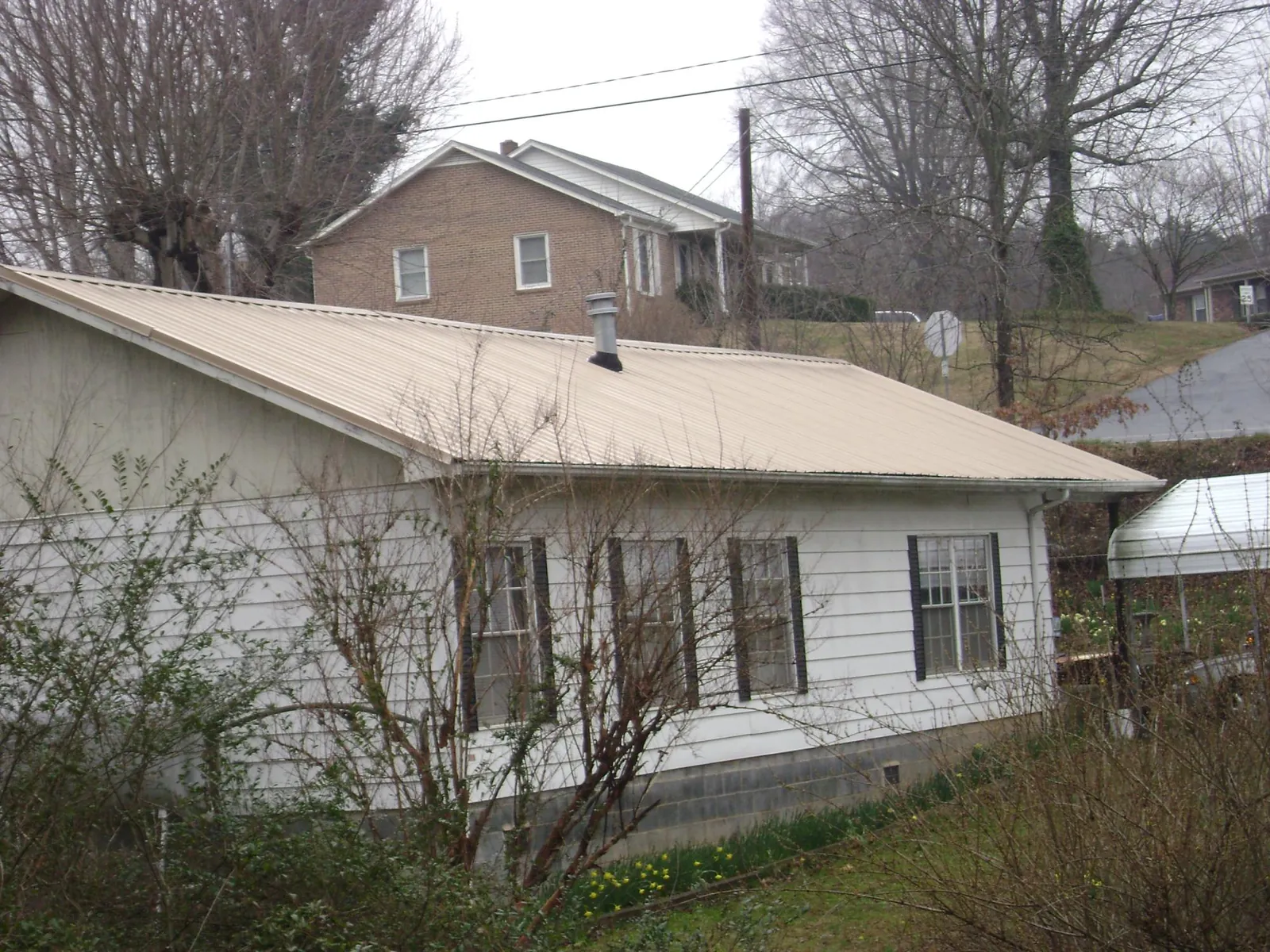 Tan metal roof on a white sided house set into a hillside — Commercial Roofing by Roofing Brothers in Hatch