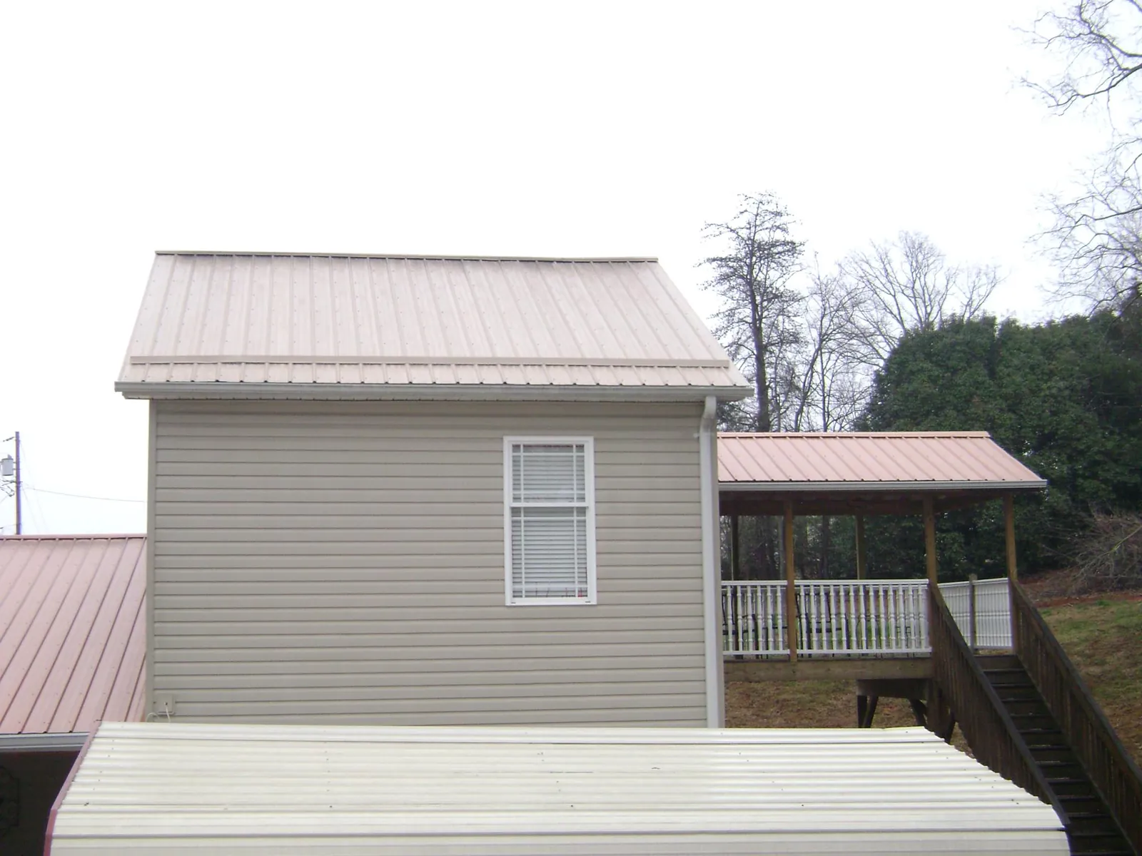 Tan metal roofs on a two story addition and attached porch, from a Roof Replacement job in Hatch